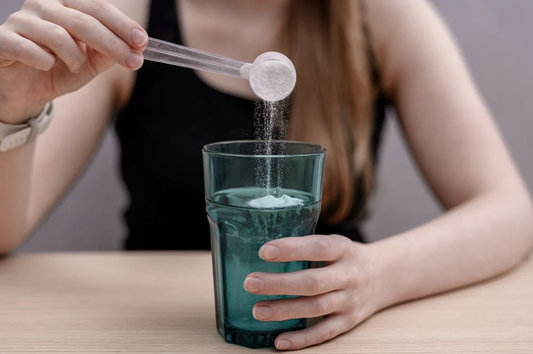 Woman scooping creatine powder into a glass of water